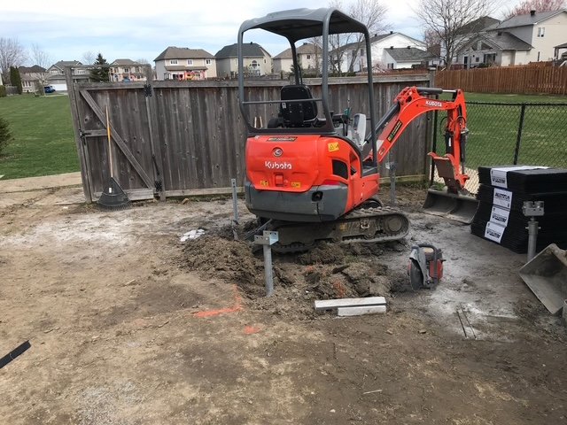 Kubota excavator driving helical piles on residential site